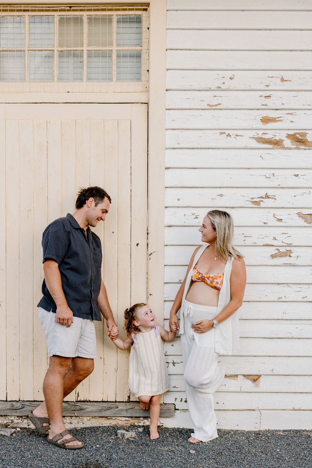 A family poses together against a rustic white wooden wall outdoors.