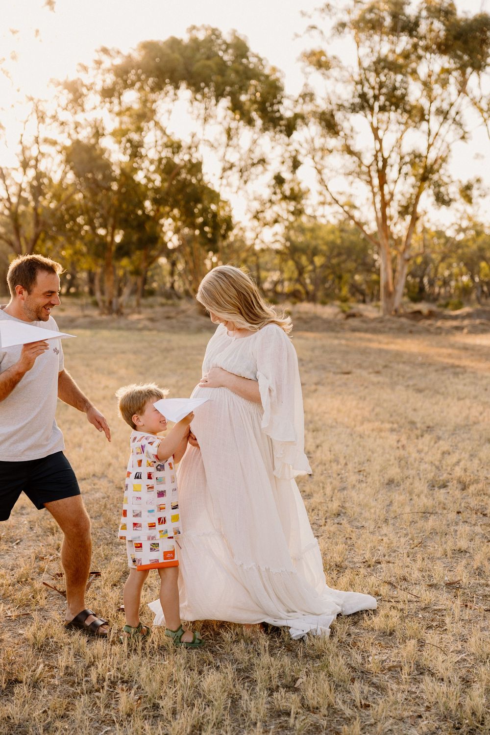 A family plays with a white sheet in an open field at sunset while wearing casual summer clothing.