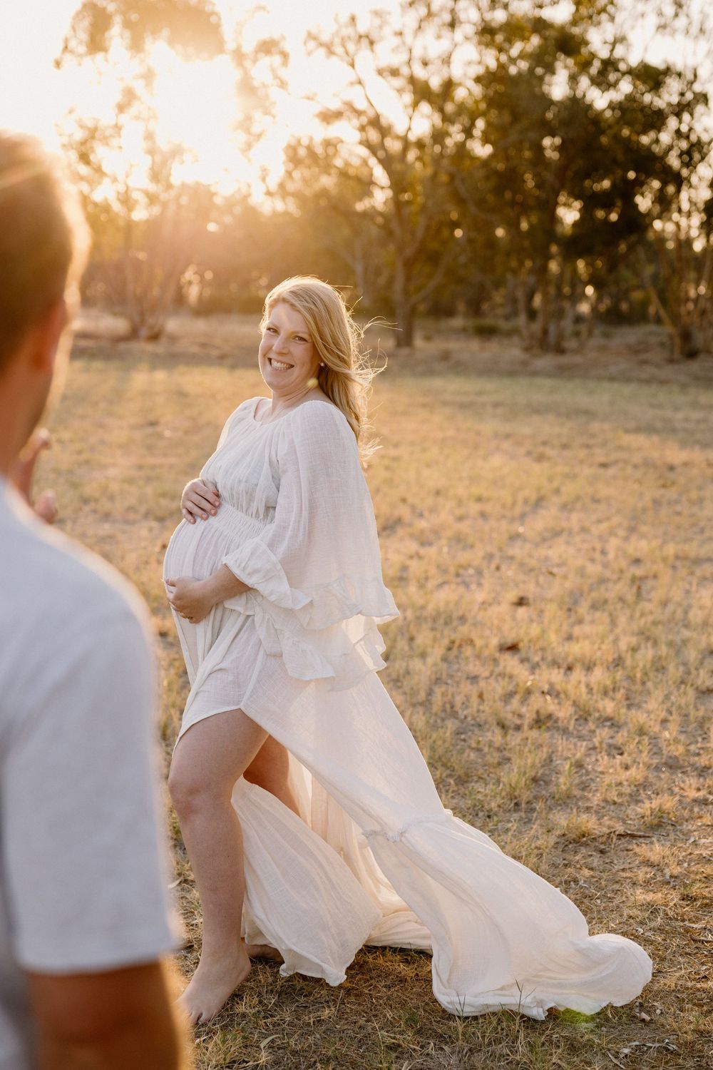Mother and child playing in a sunlit field at sunset while wearing flowing white dresses.