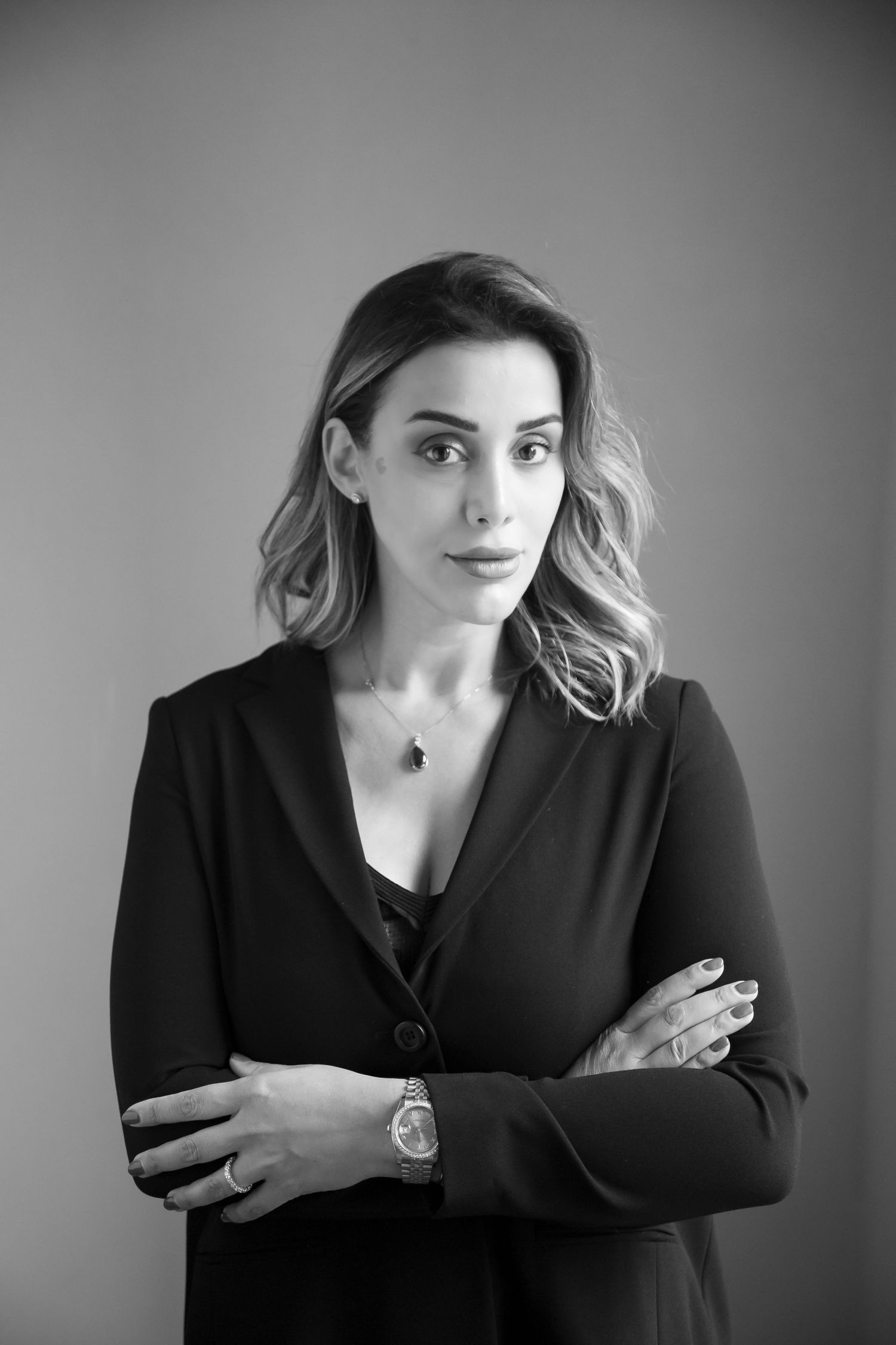 Professional studio portrait of a woman in a black blazer with crossed arms and wavy shoulder-length hair.