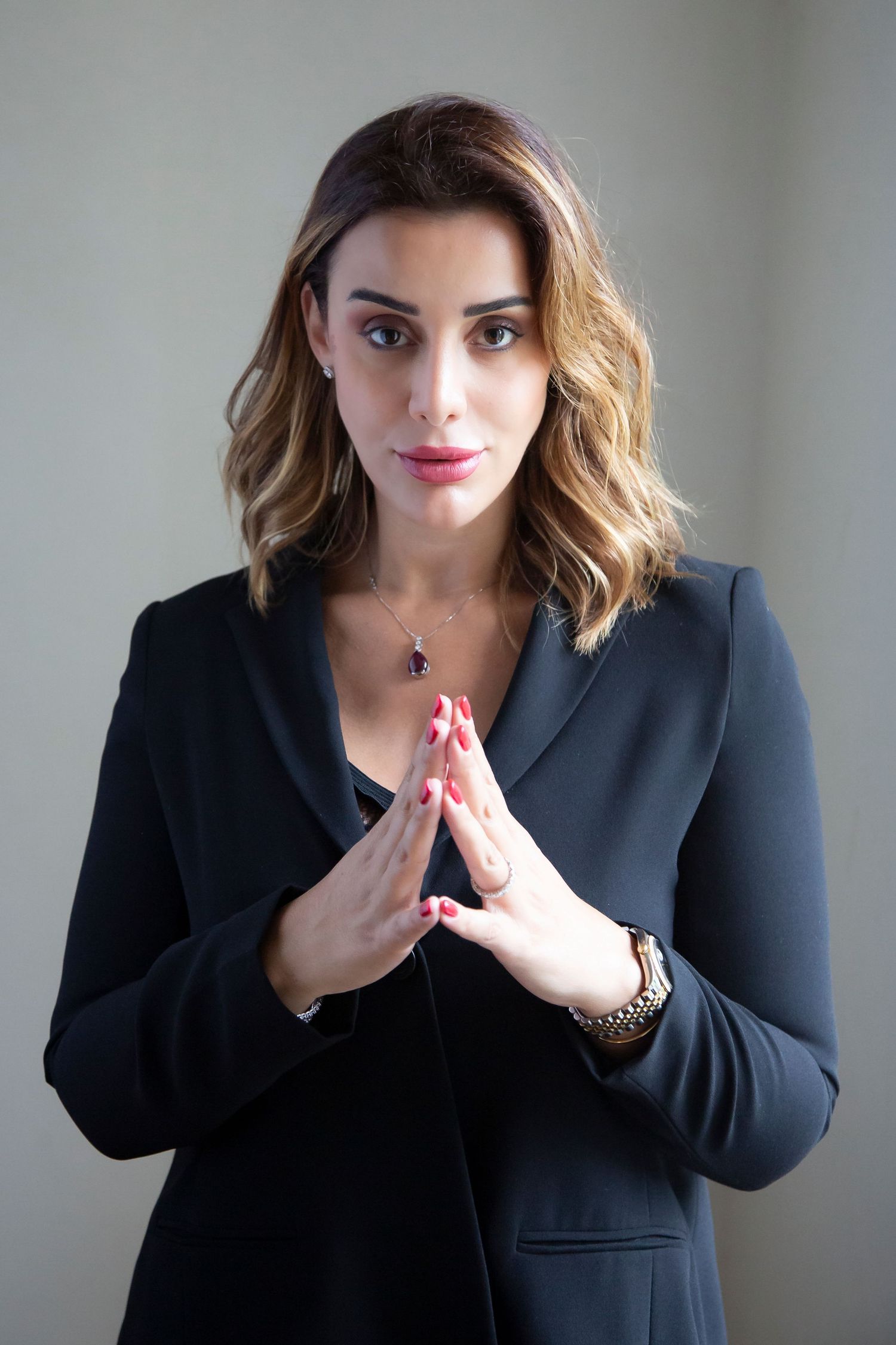 Woman in black business attire poses with hands pressed together in front of a light background.