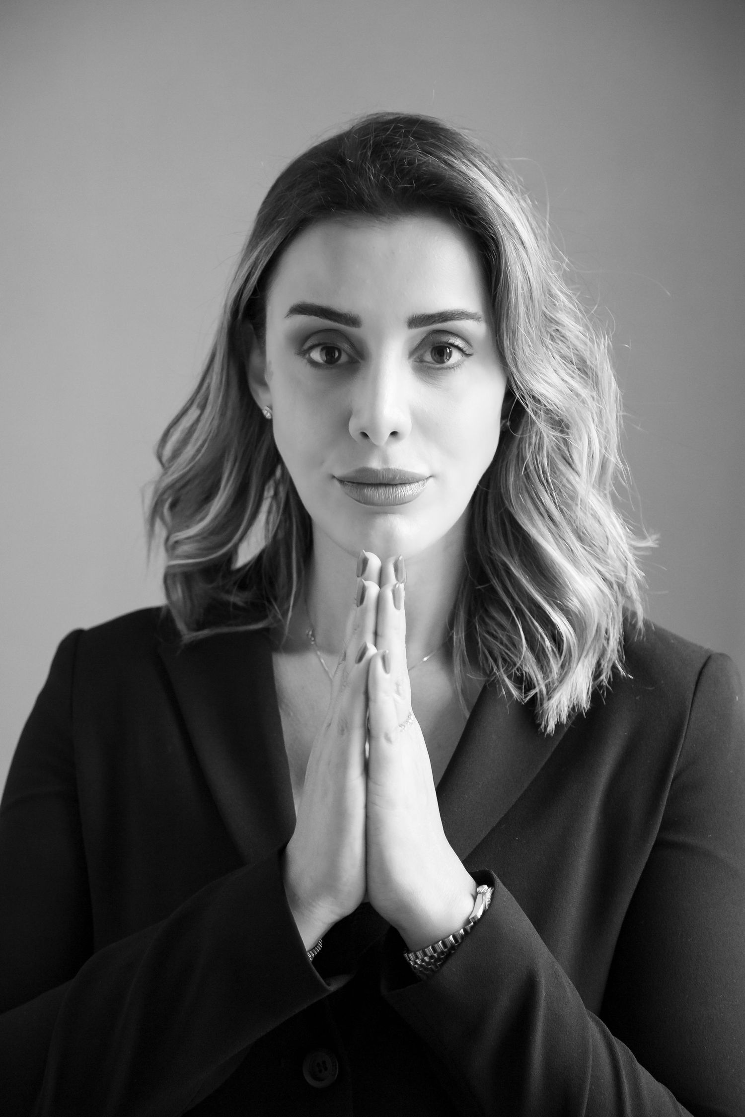 Black and white portrait of a woman in professional attire with hands clasped in prayer position.