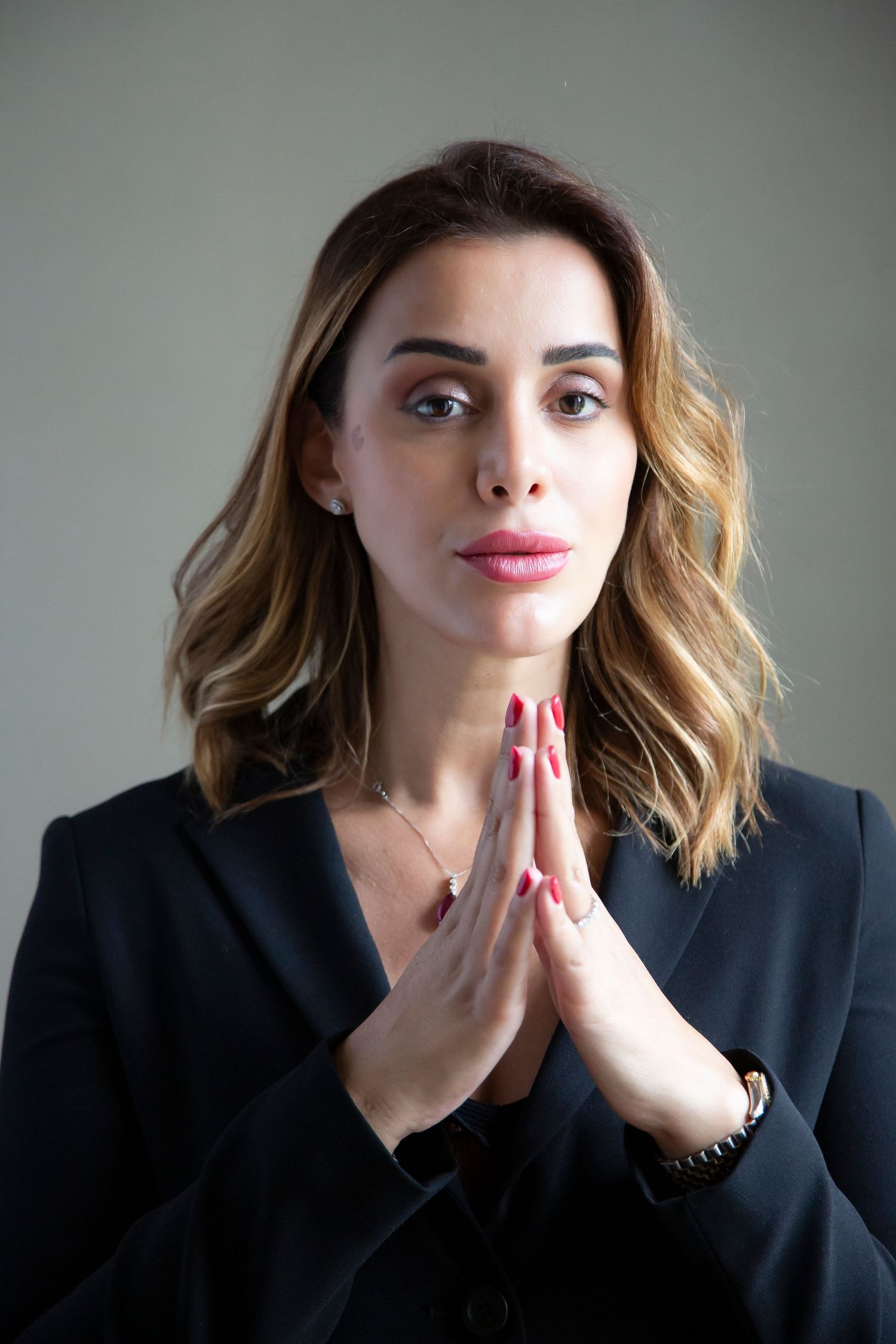 Professional portrait showing a thoughtful pose in a dark blazer with hands clasped in prayer position.