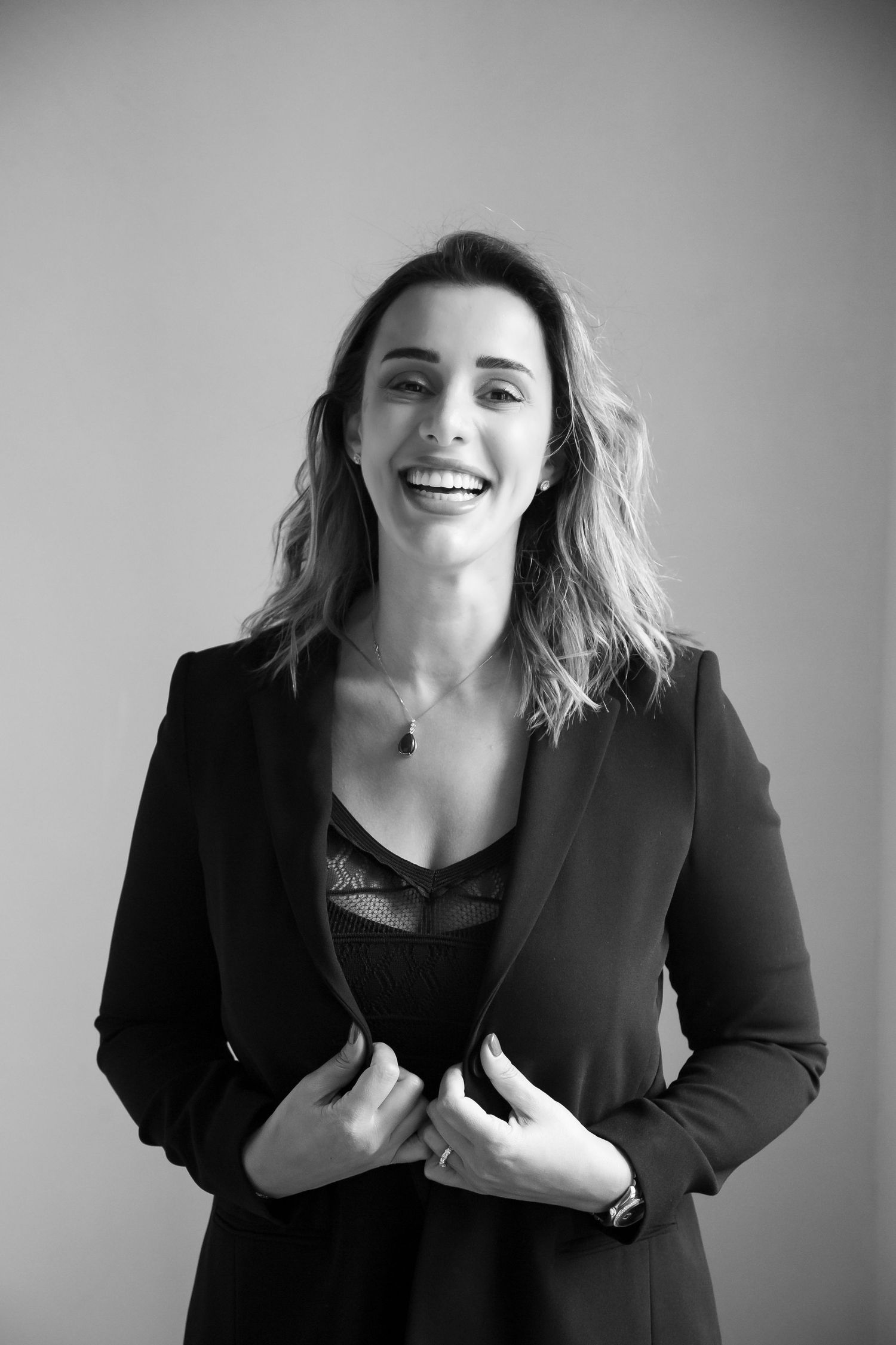 Black and white portrait of someone wearing a black blazer and lace top while smiling.