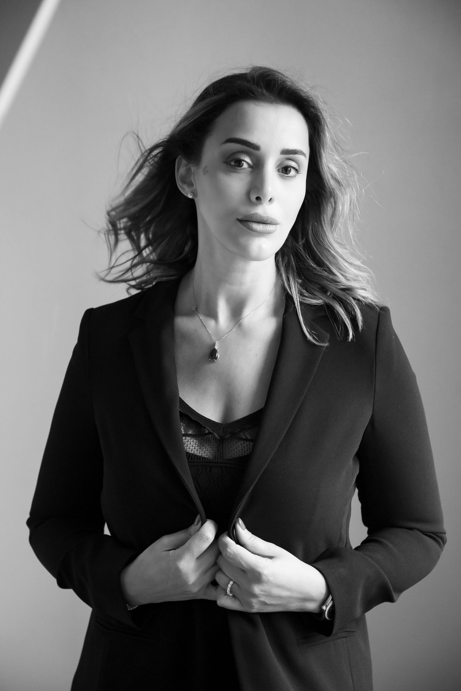 Professional portrait of a person in a black blazer with tousled hair against a gray background.