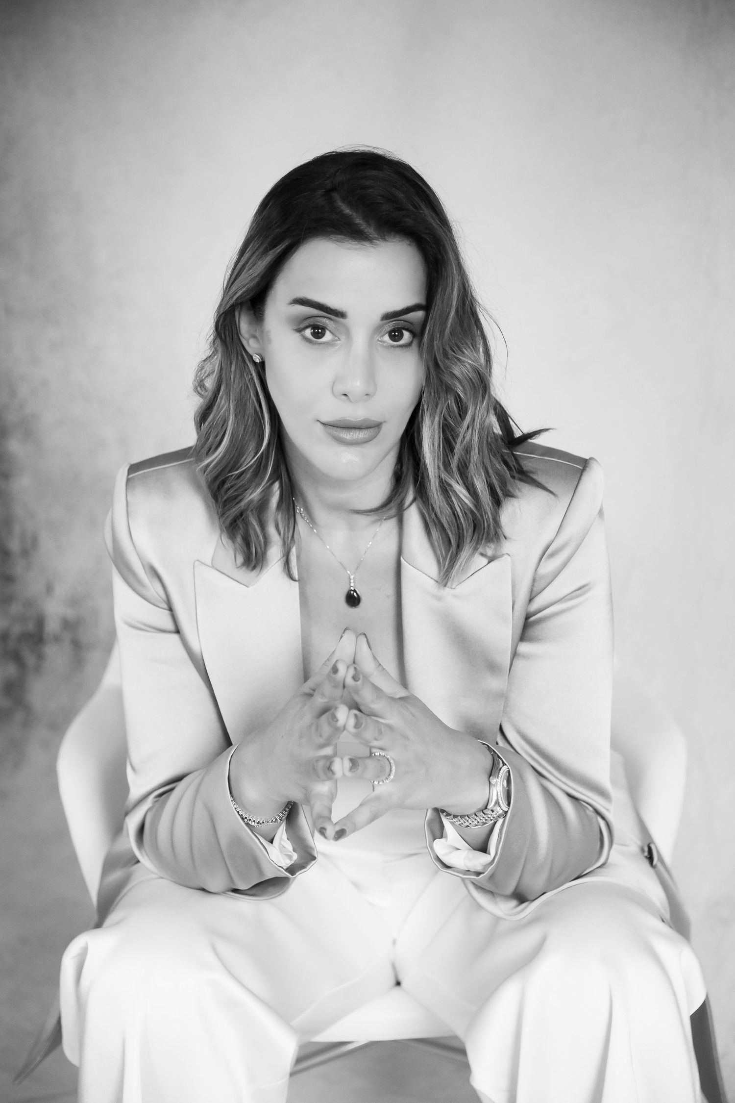Black and white portrait of someone in a light colored blazer sitting with clasped hands.