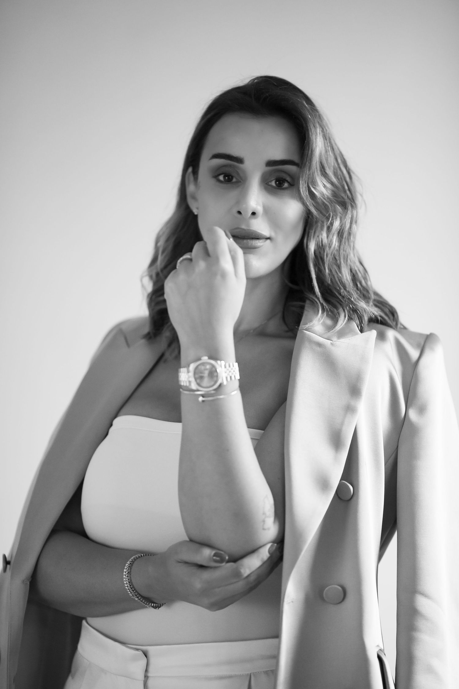 Black and white portrait of a woman in a white crop top and blazer wearing a statement watch.