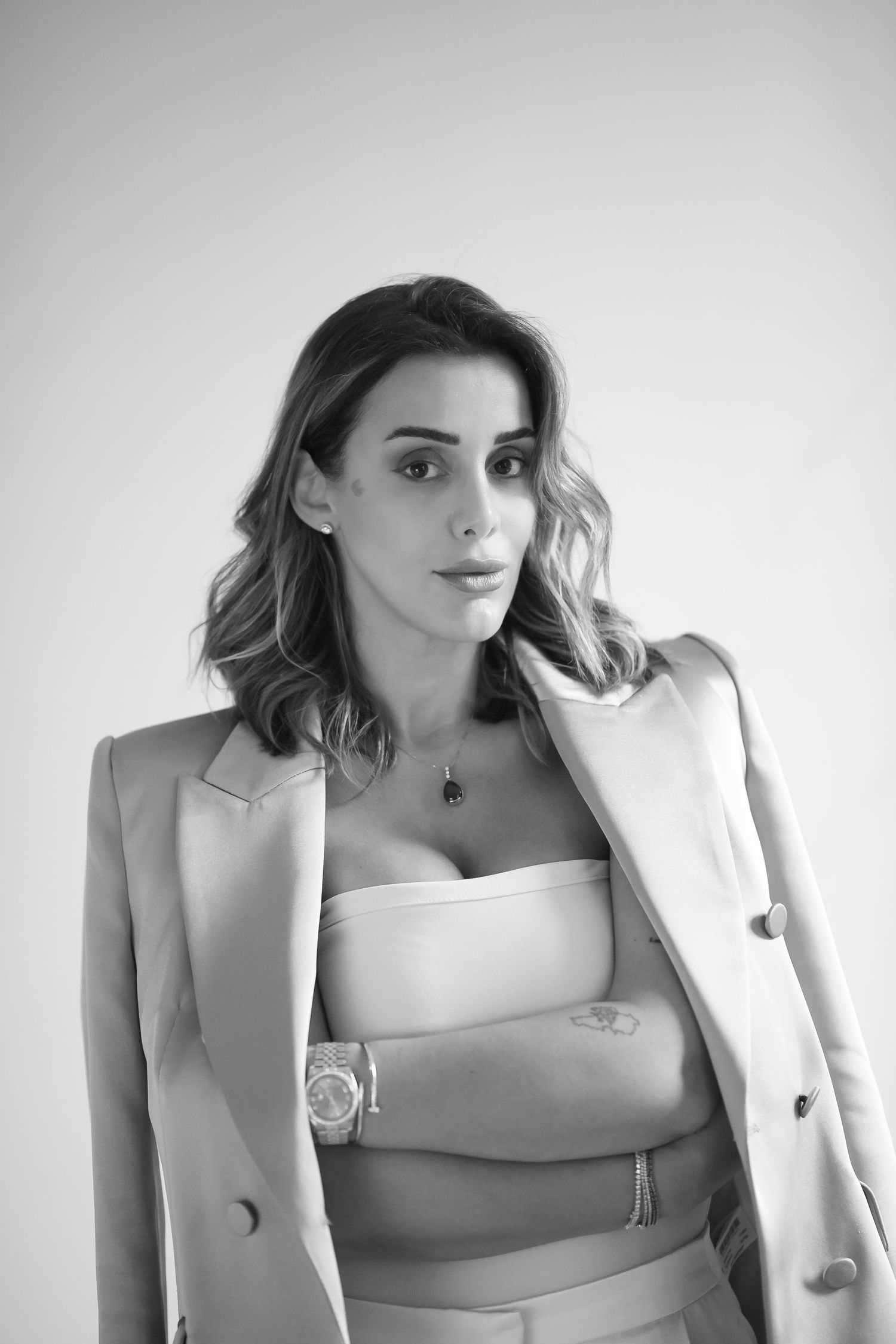 Studio portrait featuring someone in a beige blazer and white crop top against a gray background.