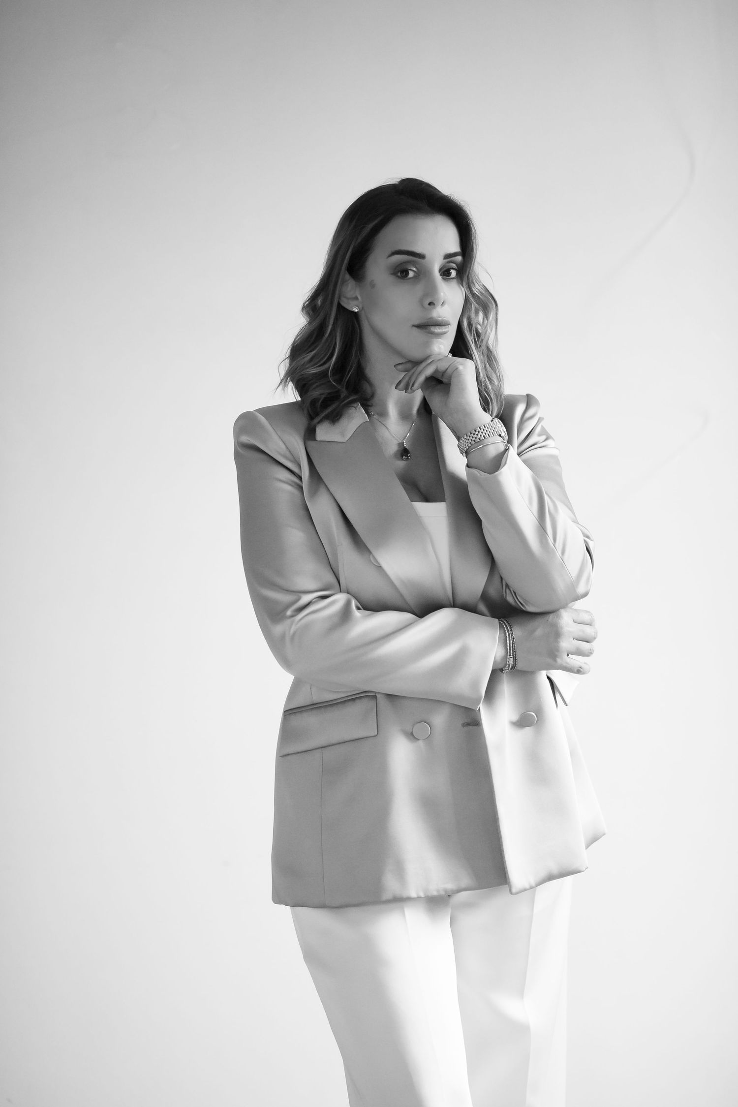 Professional portrait of someone in a light blazer and white pants with contemplative pose.