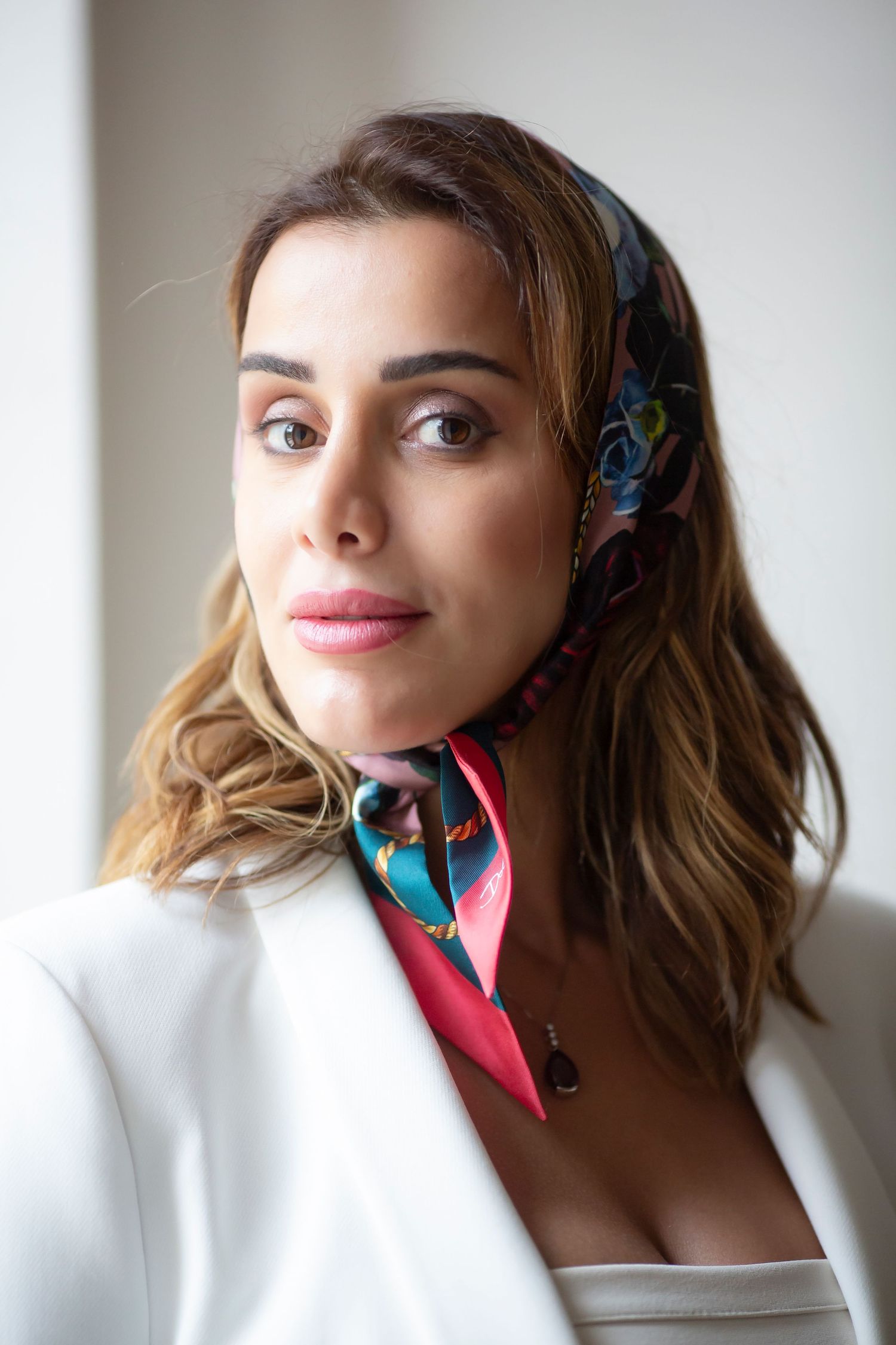 Fashion model wearing a white blazer and colorful patterned silk scarf in a studio portrait.