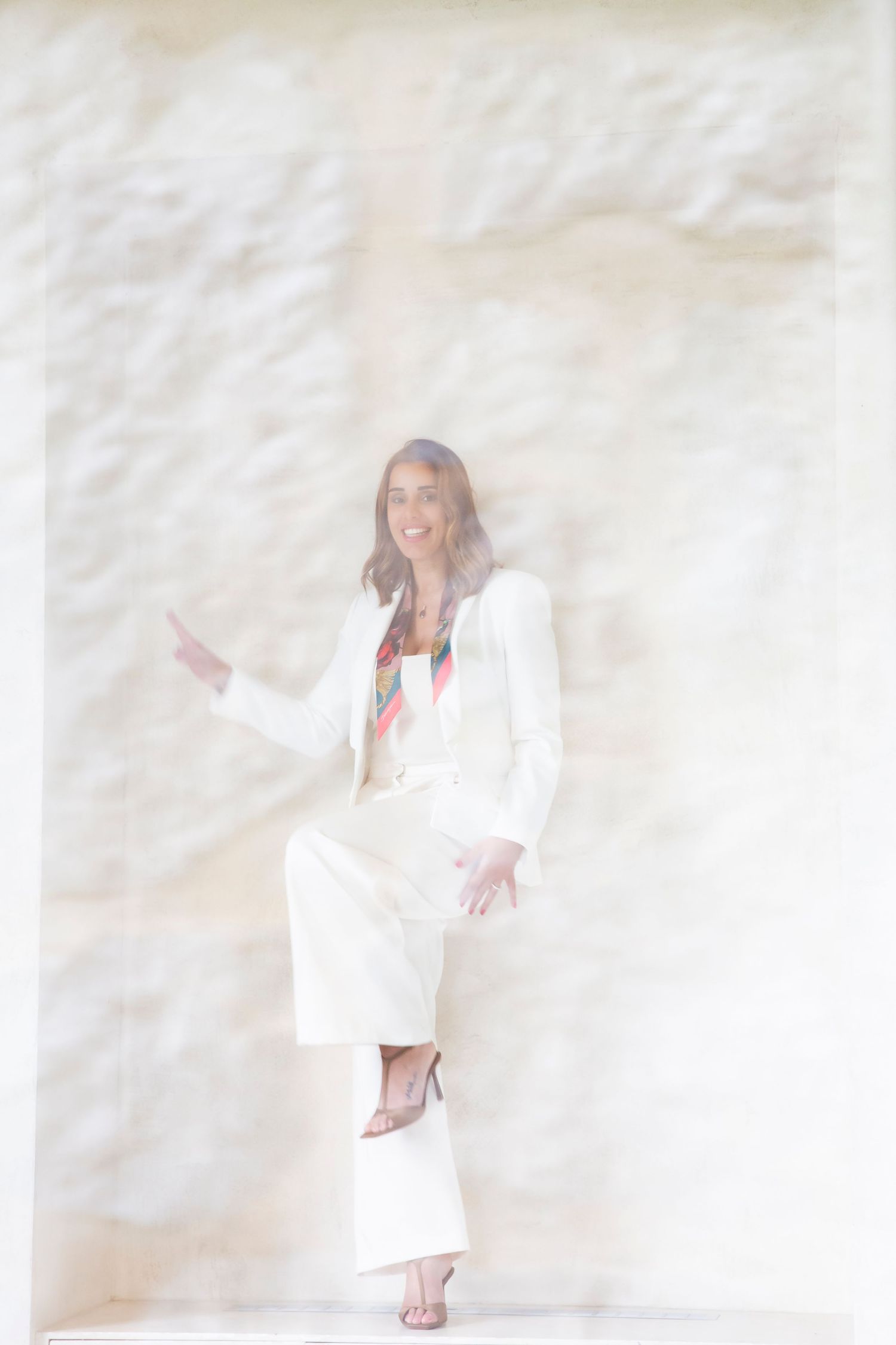 Professional fashion photo of a woman in an all-white pantsuit standing against a textured light background.