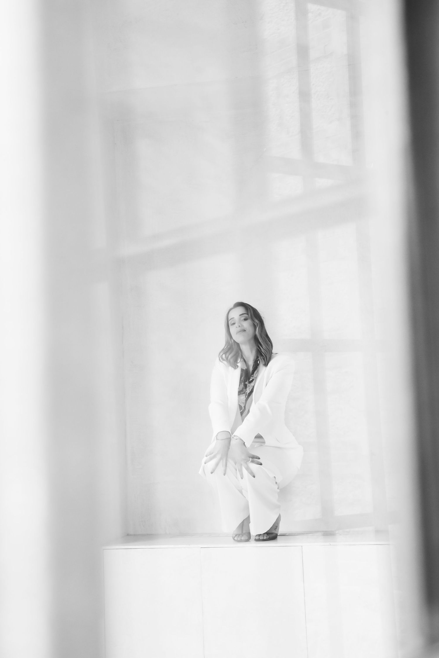 Artistic black and white portrait with dramatic window lighting and minimalist composition.