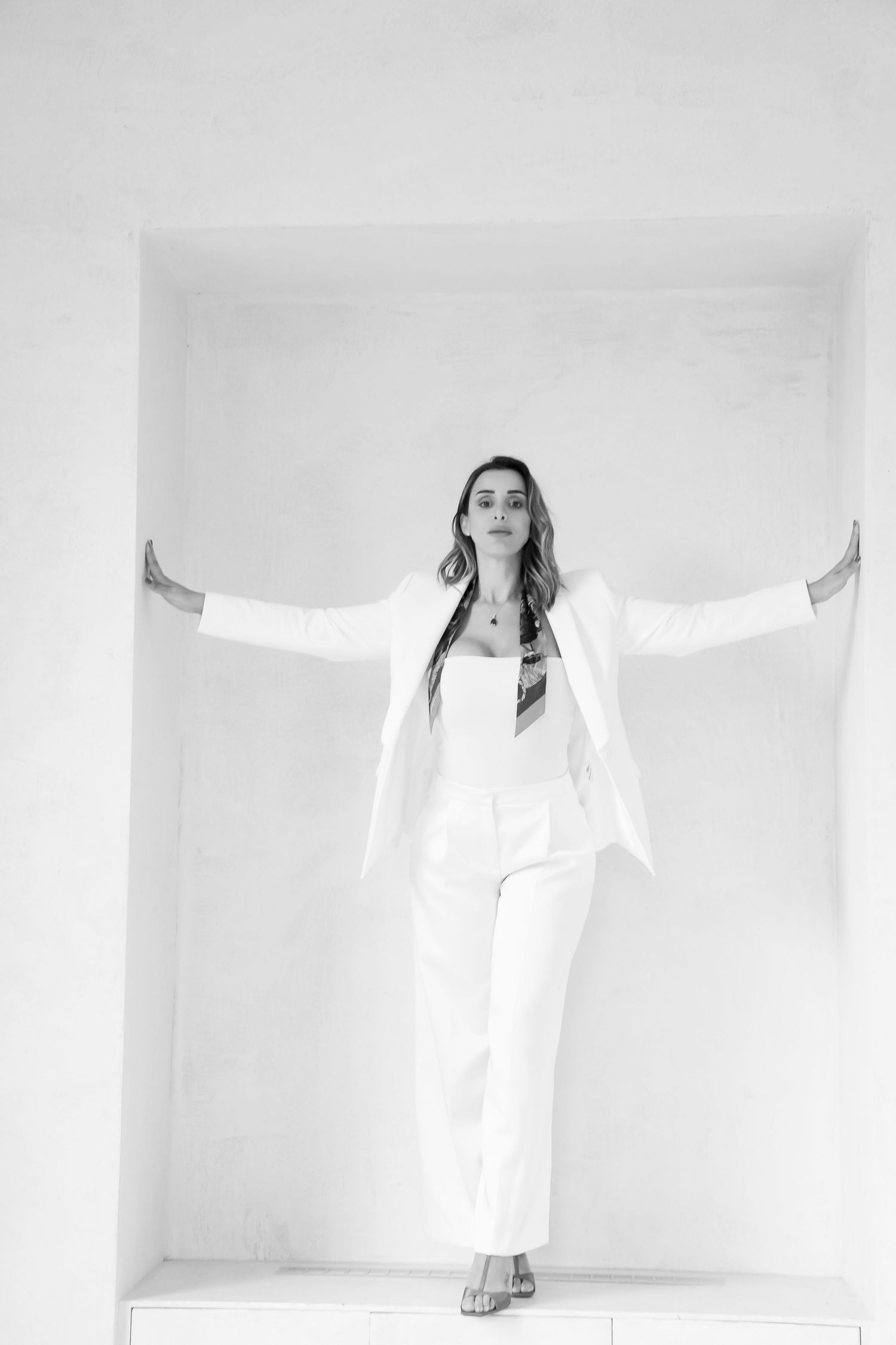 Minimalist black and white photo showing confident pose with arms outstretched in white outfit.