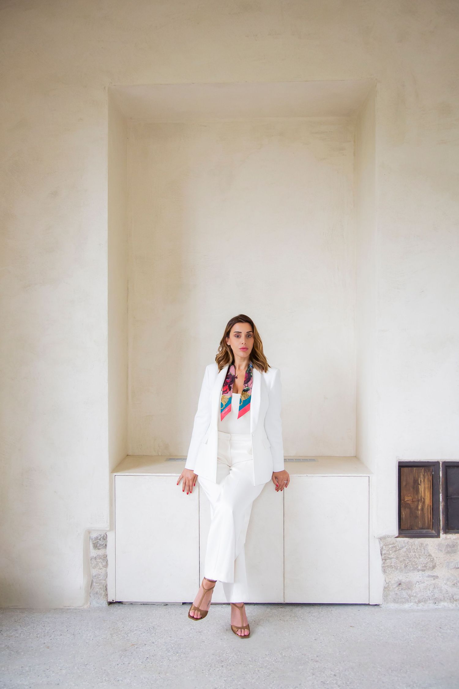 Person in white suit with colorful accent scarf standing in modern minimal interior space.