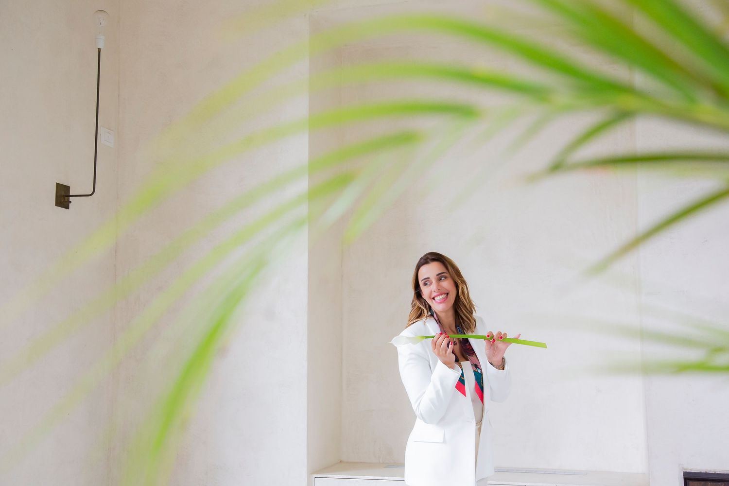 A person in a white shirt stands against a light wall with palm leaves creating shadows in the foreground.