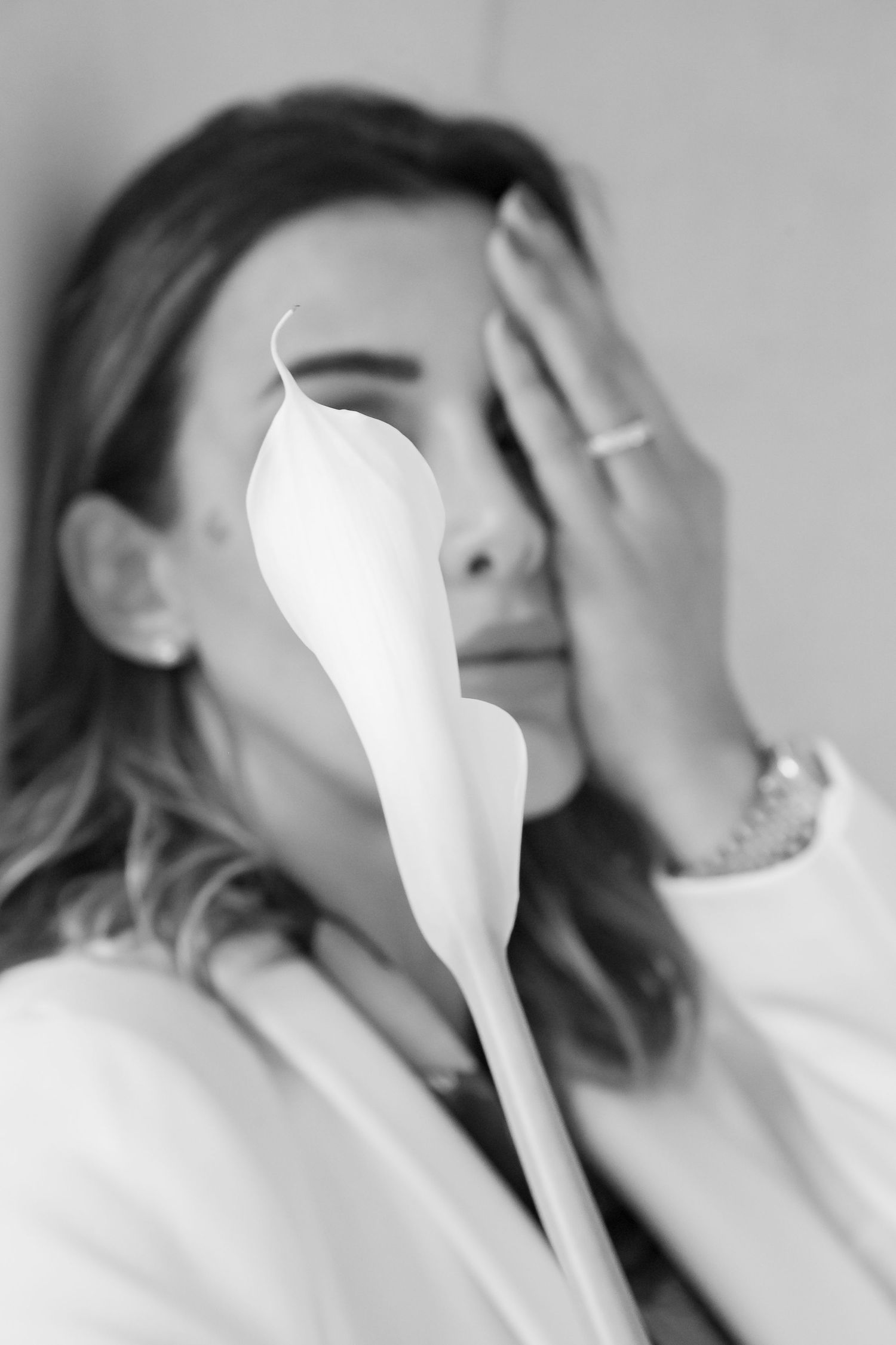 Artistic black and white photo of a person holding a white calla lily in front of their face.