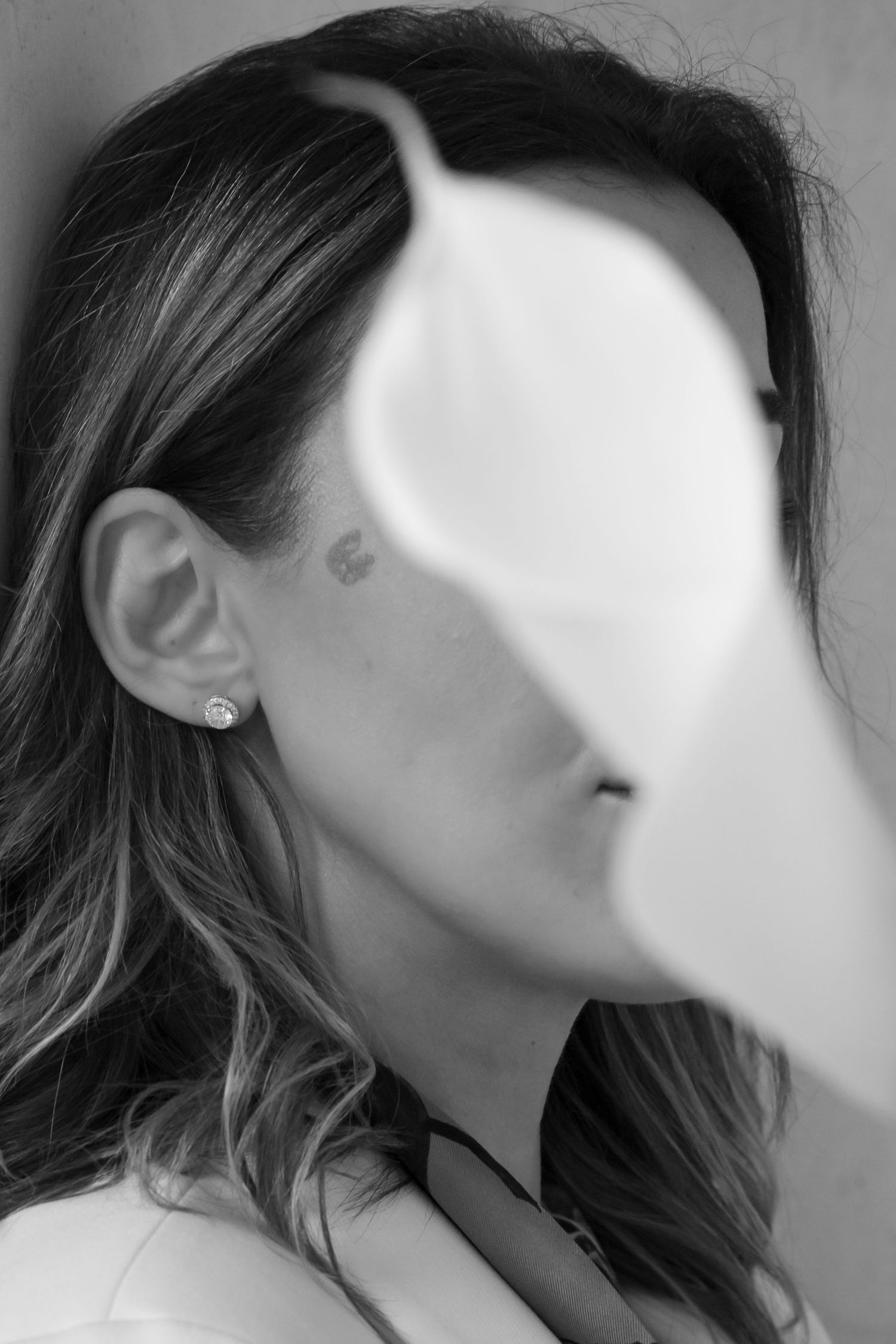 Black and white portrait of someone with wavy hair and an earring, with half their face obscured by a white overlay effect.