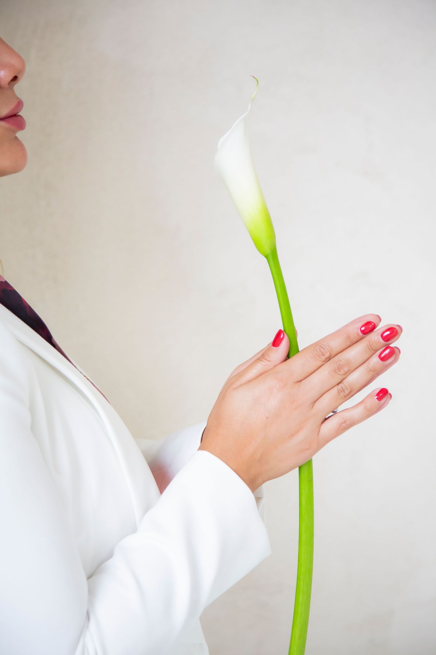 Person in white holding a single calla lily flower against a light background with red nail polish.