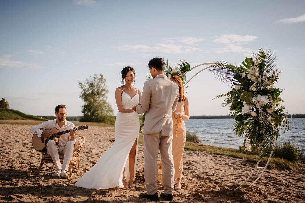 Wedding ceremony guests sit on the beach at sunset while overlooking a calm lake with vibrant evening skies.