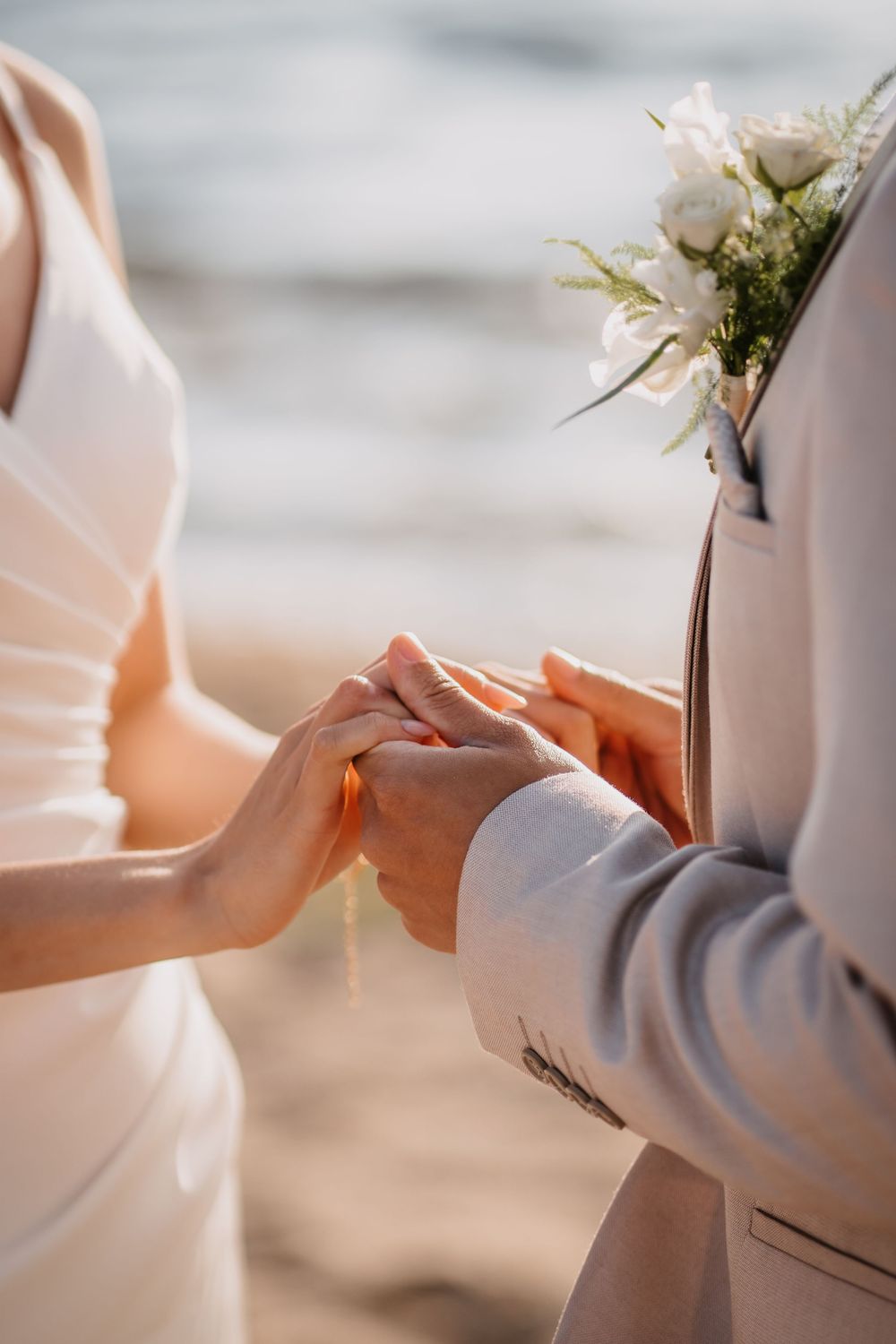 Close-up view of hands exchanging wedding rings during an intimate beach ceremony ceremony with soft lighting and delicate details.