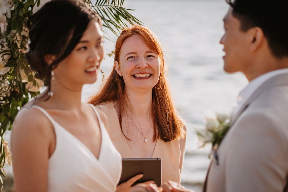 Five wedding party members laugh together outdoors during a sunset ceremony by the ocean.