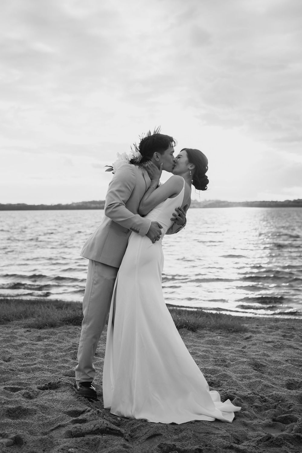 A romantic black and white beach wedding photo shows a couple kissing at sunset by the water's edge.
