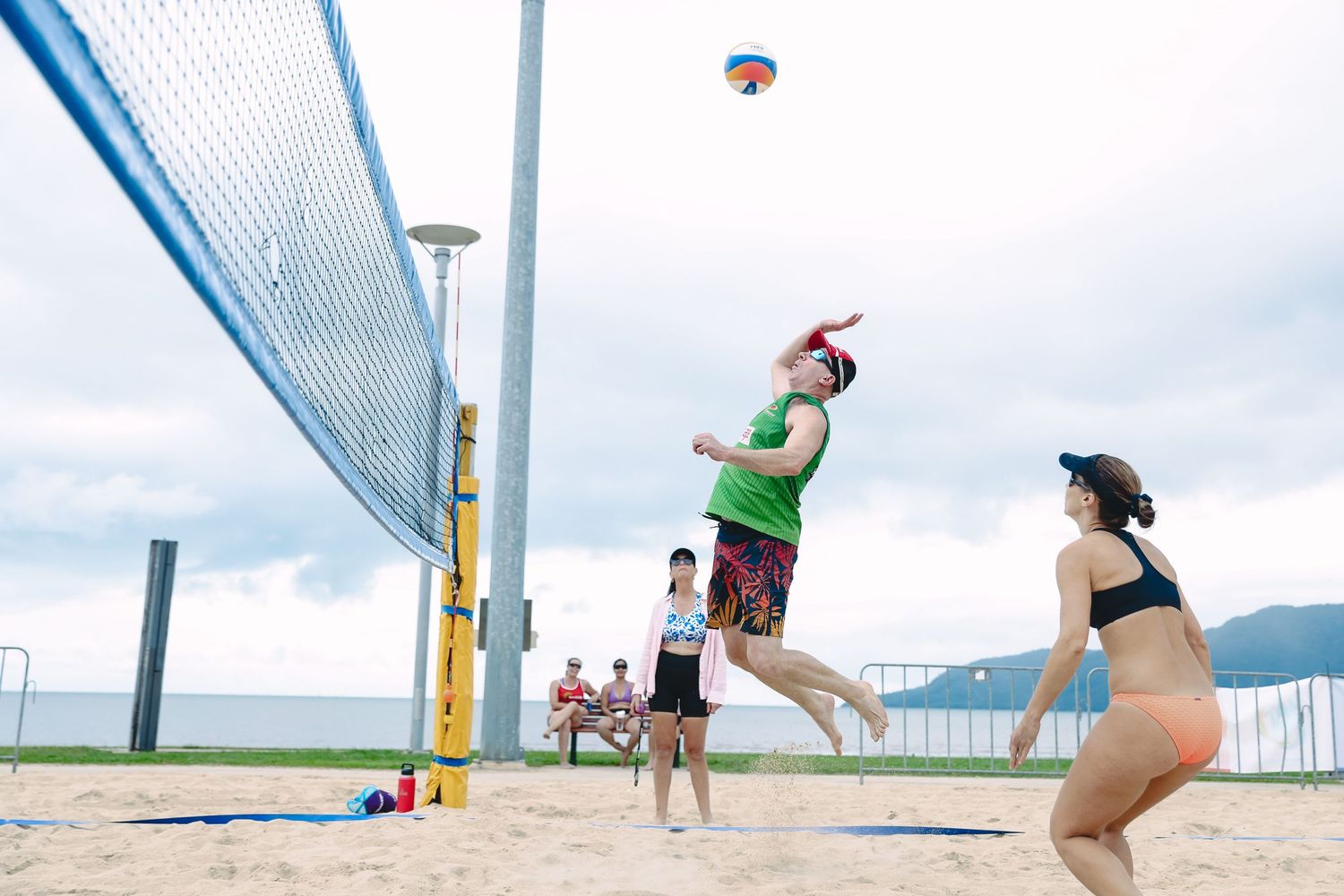 A row of six beach volleyball players jumping to hit balls over a net on a sunny outdoor court.