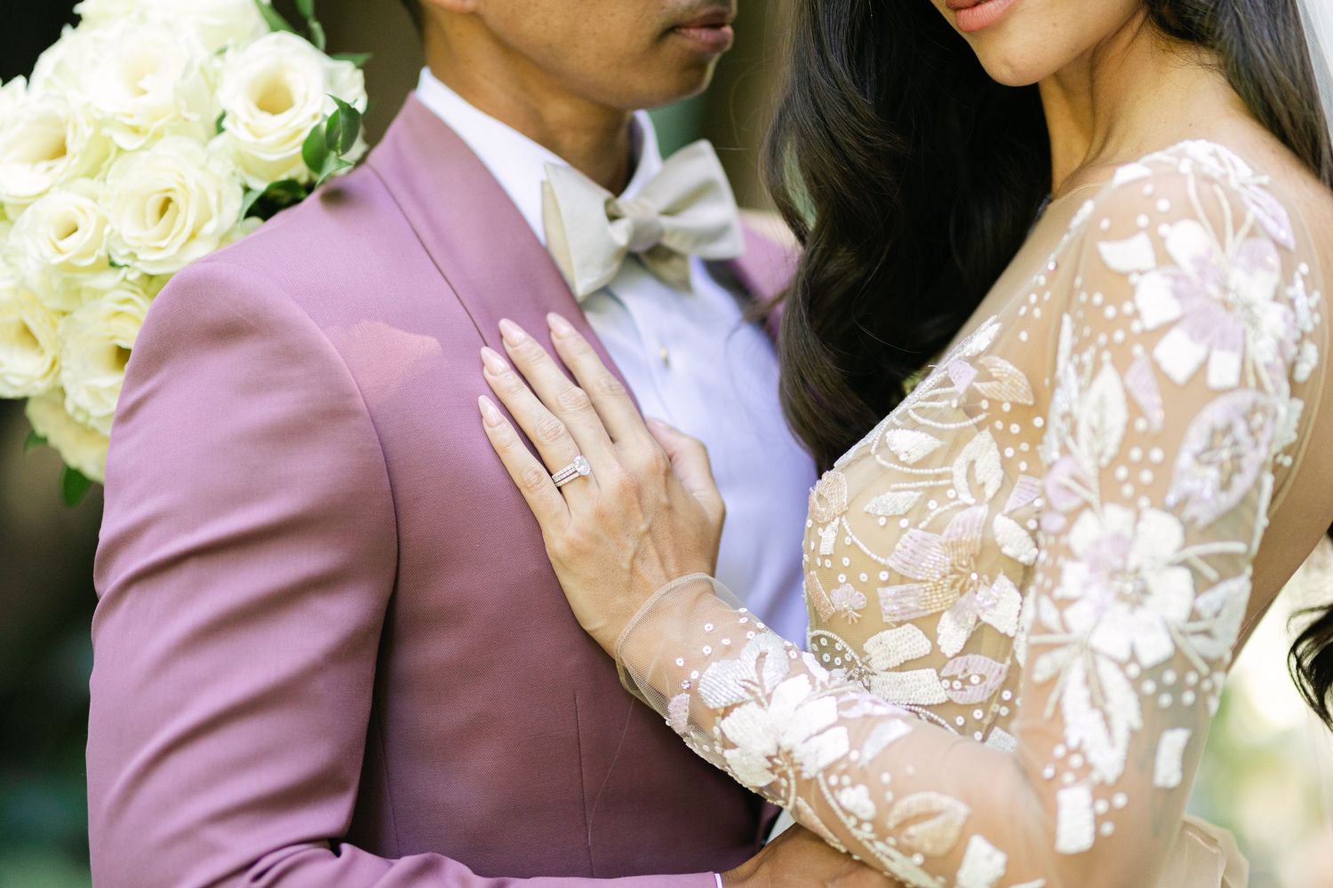 A newlywed couple shares romantic moments in a garden setting with white florals and pink and mauve tones.