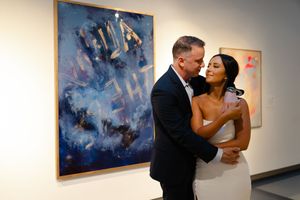 Couple dancing close together in an art gallery with abstract blue paintings displayed on white walls.