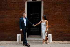 A couple poses against a brick wall with natural lighting during a wedding photo shoot.
