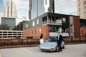 Grey Porsche parked in front of modern brick and glass buildings in an urban setting.