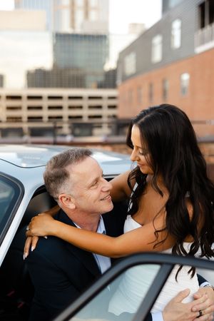 Bride and groom embrace in romantic moment near luxury car at an urban wedding venue.