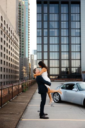 A romantic dance sequence between a couple in formal attire near a modern building and parked car.