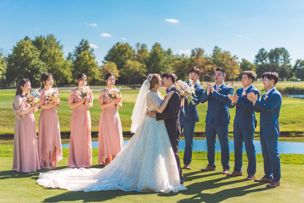 Wedding party in pink dresses and blue suits posing together on a golf course.