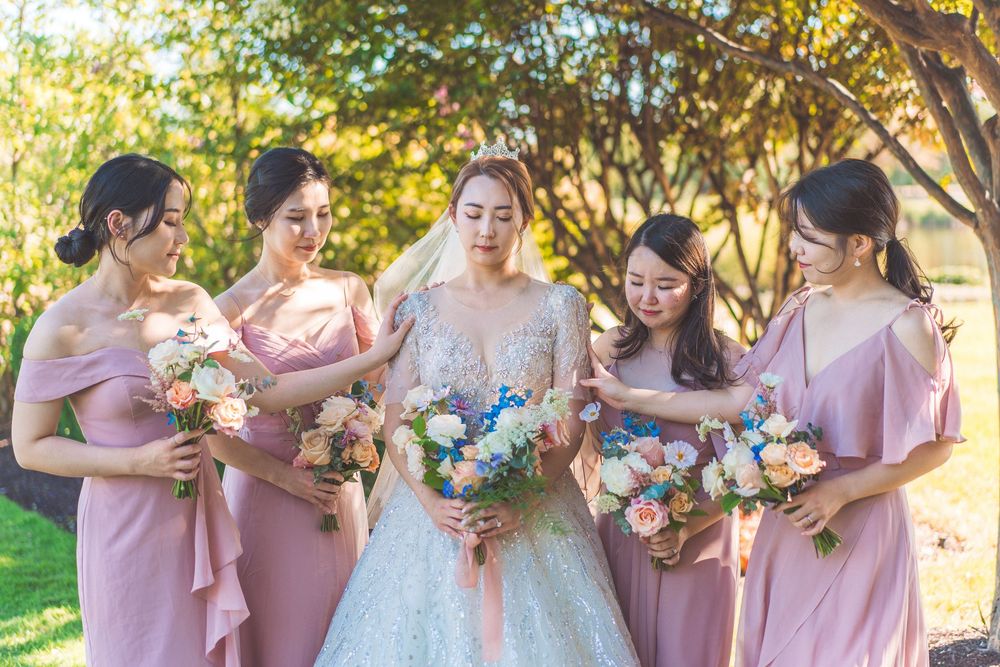 A bridal party in pink dresses poses with bouquets in a garden setting on a sunny day.