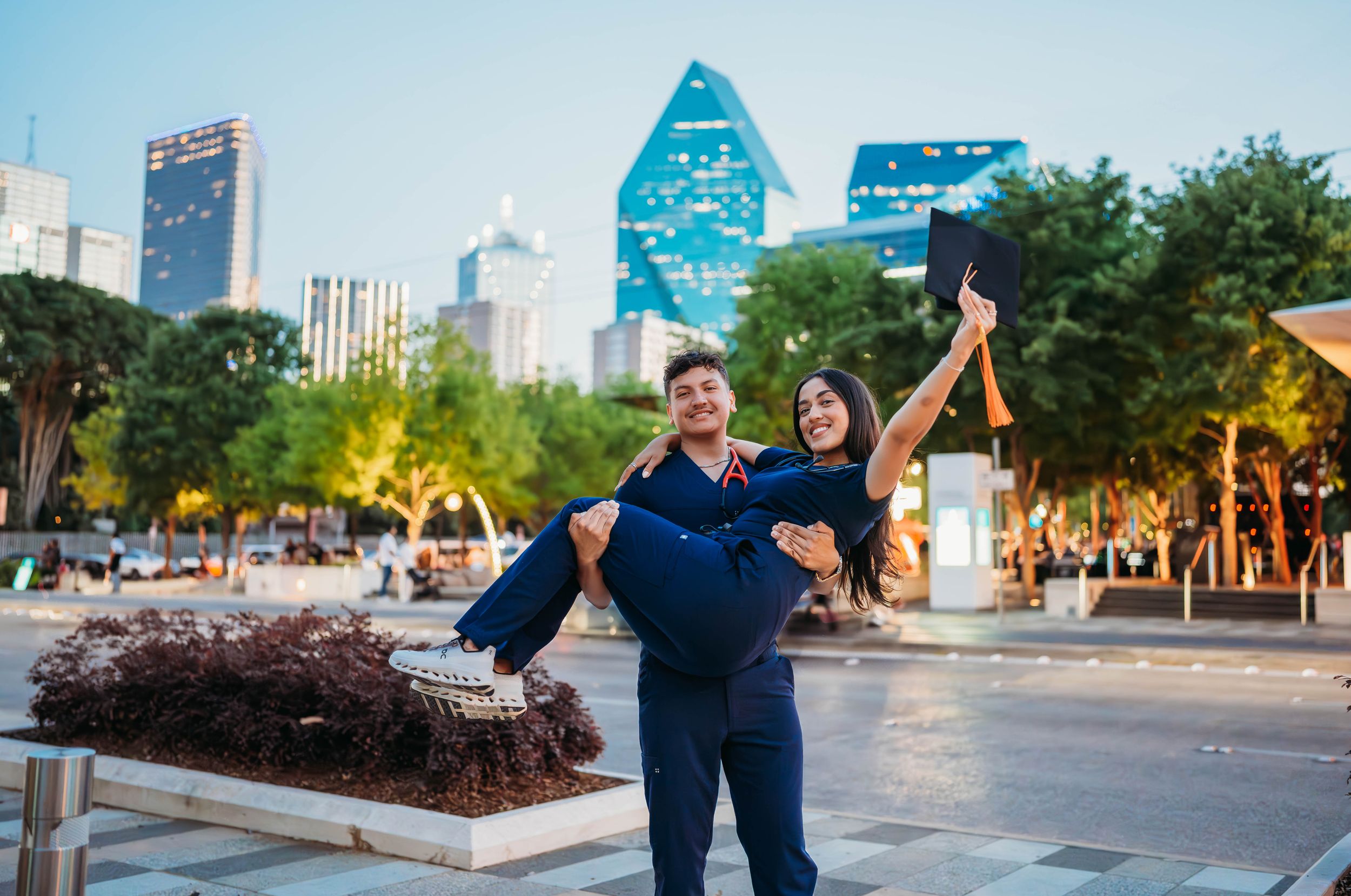 Medical professionals in navy scrubs celebrate together in front of a city skyline at dusk.