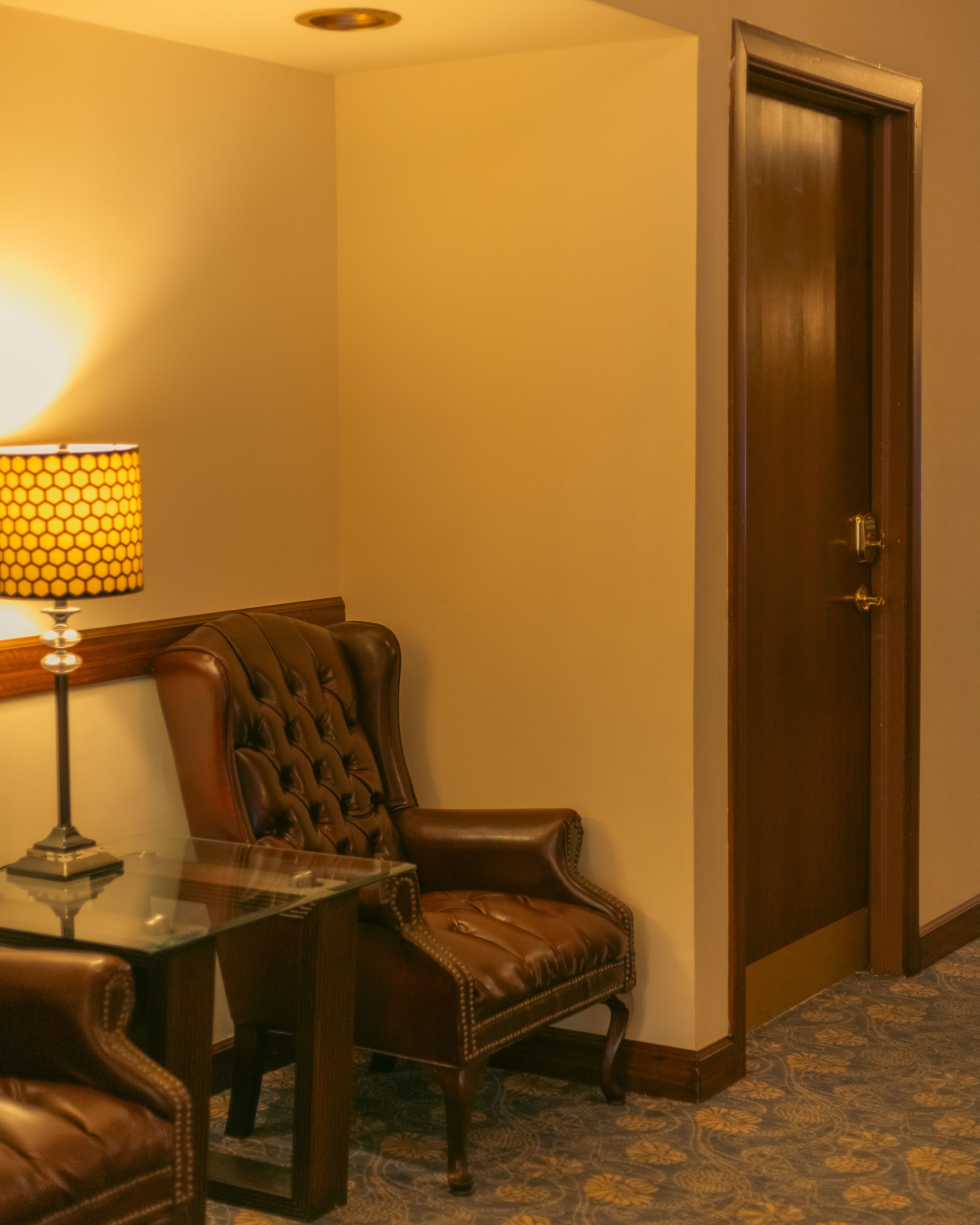 Hotel hallway with brown leather chairs, patterned carpet, and warm lighting from wall sconces.