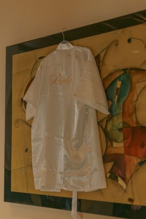 White wedding dress shirt hangs on display against decorative wall art.