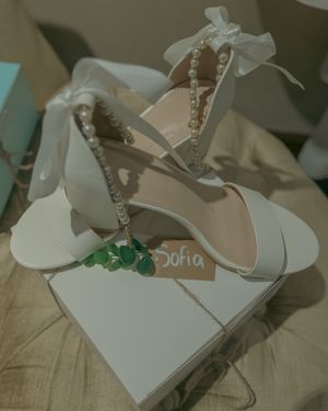 White bridal shoes with pearl embellishments displayed on beige surface.