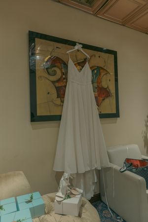 White wedding dress displayed on hanger against wall with framed artwork.