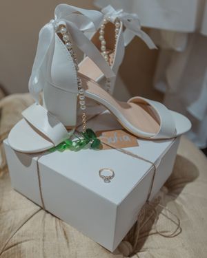 Elegant white bridal shoes with pearl details in display box.