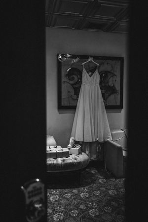 Black and white photo of wedding dress hanging in dimly lit room.