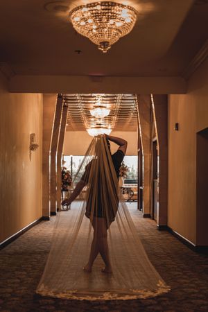 A dramatic silhouette in a long dress stands in an elegant hotel hallway with crystal chandeliers.