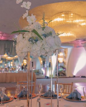 Wedding reception tables decorated with tall white floral centerpieces and wooden chairs.
