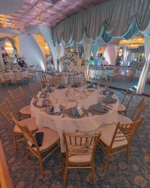 A wedding reception venue with wooden chairs and white tablecloths set up for celebration.