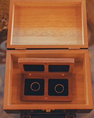 Wooden box with velvet-lined compartments displaying wedding rings on dark cushions.