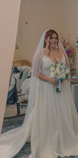 Elegant white wedding gown with flowing train and veil photographed in preparation room.