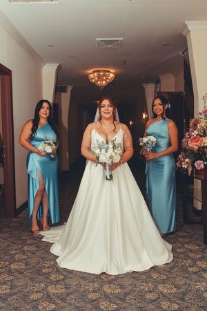 Wedding party in blue bridesmaid dresses and white bridal gown posed in hotel hallway.