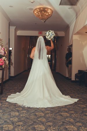 Dramatic train of white wedding dress spread out on patterned carpet.