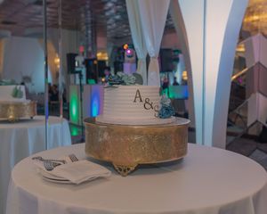 An elegant wedding cake display on a white table with white draping and colorful lighting in the background.
